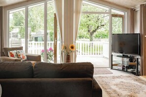 A living room with a sofa, a television, and a view of a backyard through large sliding glass doors. - Cosy Lodge on Farm with Donkeys, Parking (Chester)