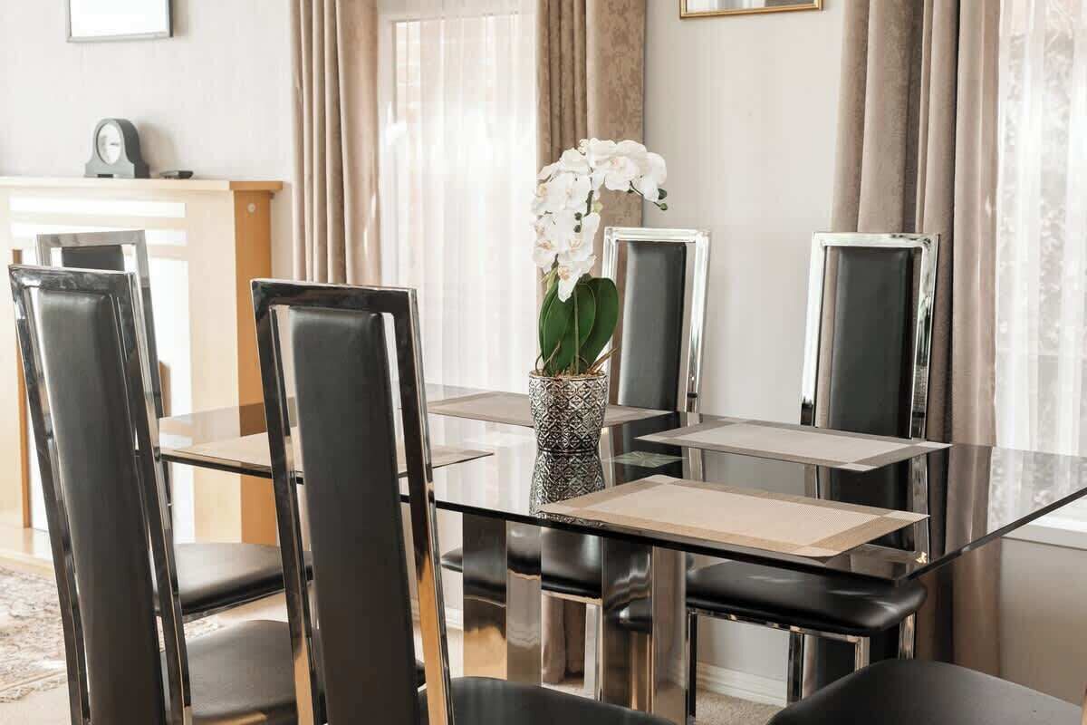 A dining area with a glass table, black chairs, and a vase with white flowers.
