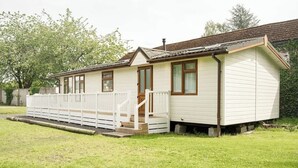 A small, single-story building with a porch and a fenced area. - Cosy Lodge on Farm with Donkeys, Parking (Chester)