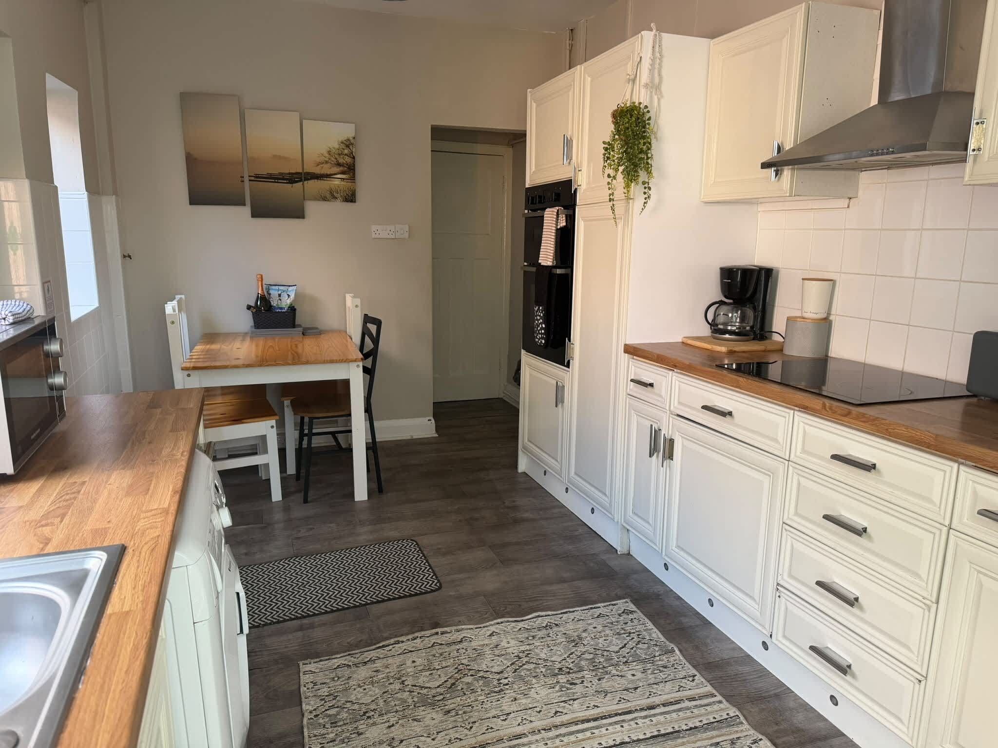 A kitchen with white cabinets, a wooden countertop, a coffee maker, and a refrigerator.