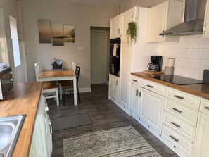 A kitchen with white cabinets, a wooden countertop, a coffee maker, and a refrigerator.