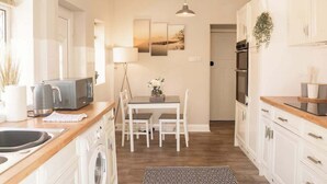 A modern kitchen with white cabinetry, a dining table with chairs, a hanging light fixture, and a refrigerator. - Budget friendly Edwardian home - Sleeps up to 7 (Cheshire West and Chester)