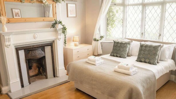 A bedroom with a fireplace, a bed with pillows, a nightstand with a lamp, and a window with curtains. - Budget friendly Edwardian home - Sleeps up to 7 (Cheshire West and Chester)