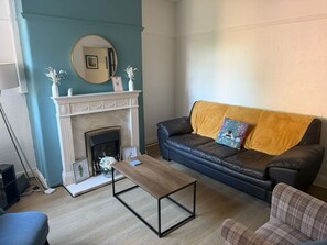 A living room with a fireplace, a sofa, a coffee table, and a blue couch. - Budget friendly Edwardian home - Sleeps up to 7 (Cheshire West and Chester)