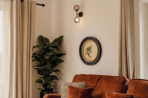 Un salón con un sofá marrón, una planta en maceta, una lámpara de pared y un cuadro enmarcado.