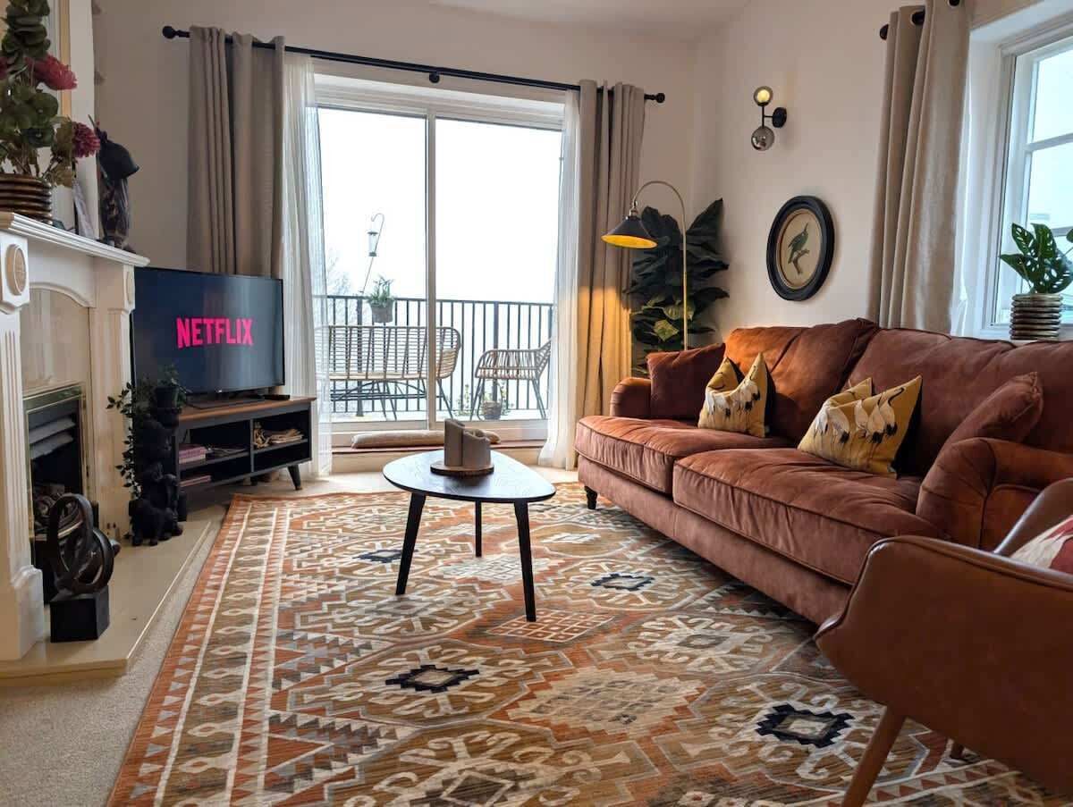 Ein Wohnzimmer mit einer Couch, einem Couchtisch, einem Kamin, einem Fernseher und einem Balkon mit Gartenmöbeln.