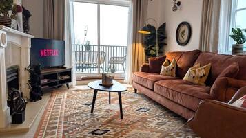Ein Wohnzimmer mit einer Couch, einem Couchtisch, einem Kamin, einem Fernseher und einem Balkon mit Gartenmöbeln.