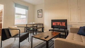A living room with a sofa, a coffee table, a TV displaying 'NETFLIX,' a window, and a door.