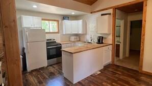 Une cuisine avec un plancher en bois, des armoires blanches, un îlot central et un ventilateur de plafond.
