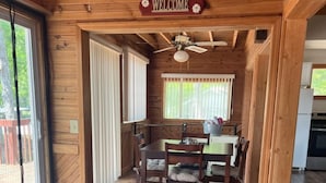 L’intérieur d’un chalet en bois, avec une pancarte « BIENVENUE », un coin repas avec une table et des chaises, et une cuisine en arrière-plan.