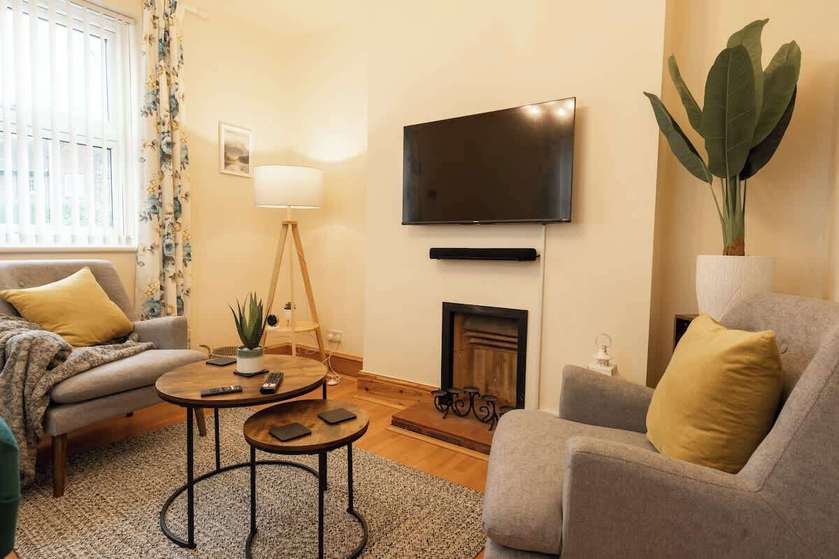 Ein Wohnzimmer mit Sofa, Sesseln, Couchtisch, Fernseher, Kamin und einer Zimmerpflanze.