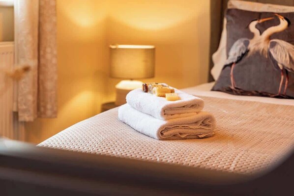 A neatly made bed with folded towels and a pillow with a bird design.