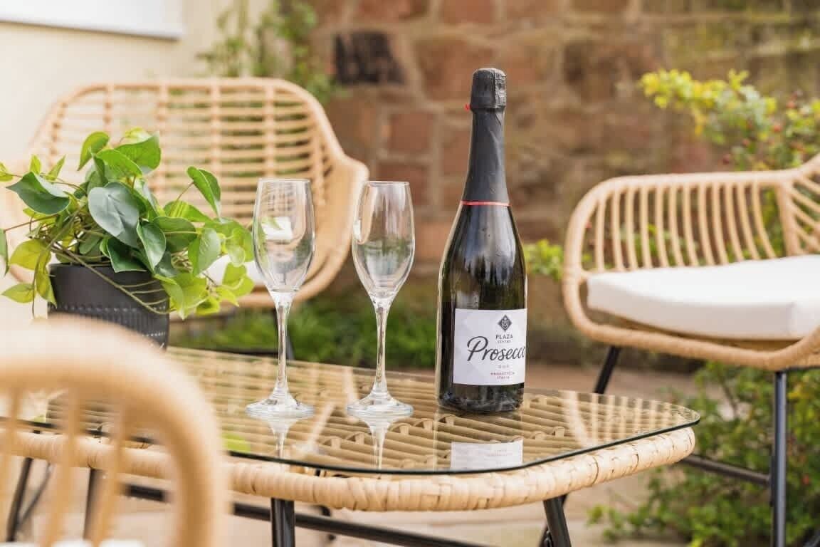 A wicker table with a bottle of wine and two glasses.