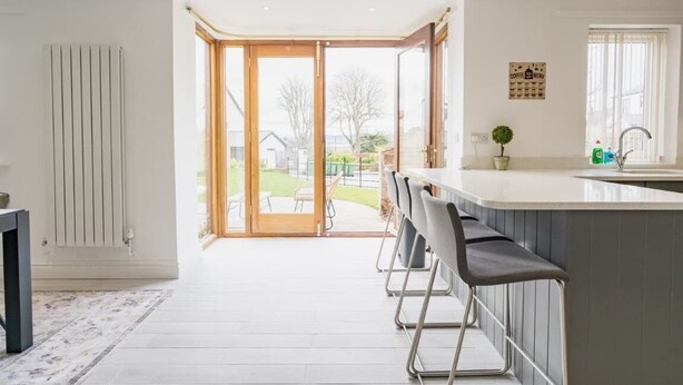 A modern kitchen with a large island, bar stools, and a view through the glass doors. - 5 Bedroom Home, Sleeps 10, Nr Royal Liverpool Golf (Merseyside)