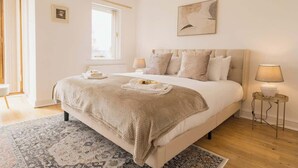 A bedroom with a large bed, a bedside table with a lamp, a window, and a framed picture on the wall. - 5 Bedroom Home, Sleeps 10, Nr Royal Liverpool Golf (Merseyside)