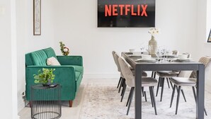 A modern living room with a green sofa, dining table, and a TV mounted on the wall displaying 'NETFLIX'. - 5 Bedroom Home, Sleeps 10, Nr Royal Liverpool Golf (Merseyside)