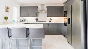 A modern kitchen with grey cabinets, a stainless steel refrigerator, and a central island with bar stools. - 5 Bedroom Home, Sleeps 10, Nr Royal Liverpool Golf (Merseyside)