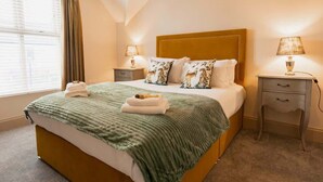 Ein Hotelzimmer mit einem Bett, zwei Nachttischen, einem fenster mit Vorhängen und einer Lampe auf einem der Tische.
