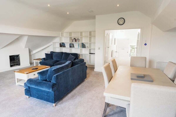 A modern living room with a blue sofa, a white dining table, and a bookshelf.