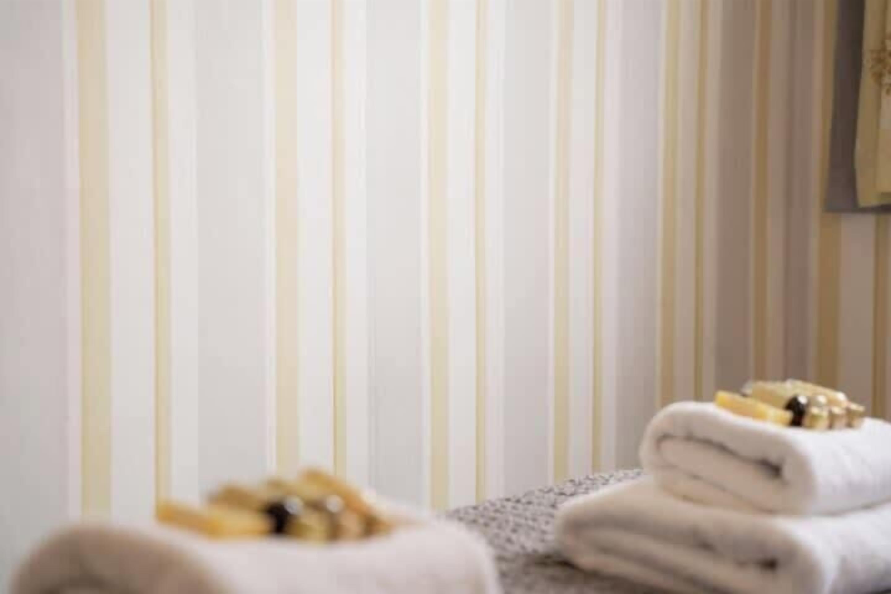 Ein Hotelzimmer mit Streifenmuster-Tapete, einem ordentlich gefalteten Handtuch und einem kleinen Tisch mit Toilettenartikeln.
