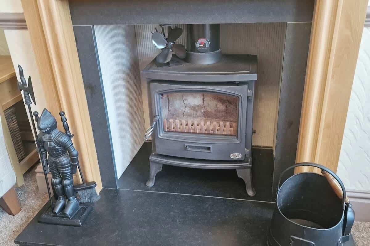A wood-burning stove with a decorative figure and a pot on the mantel.