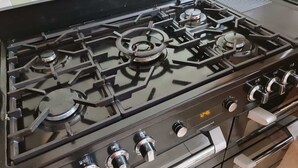 Een keuken met een gasfornuis, oven en een digitale klok waarop 12:46 staat.