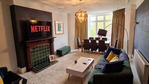 Een woonkamer met een open haard, een aan de muur bevestigde televisie, een bank, een salontafel en een eethoek met stoelen en een tafel.