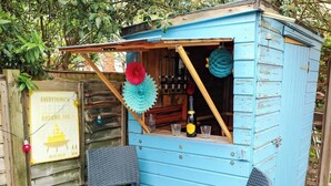 Een blauwe houten constructie met een houten tafel en stoelen, een bord en hangende decoraties.