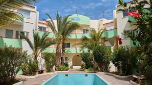 A hotel with a swimming pool, surrounded by lush greenery and palm trees.