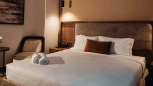 A hotel room with a large bed, a headboard with a textured pattern, a nightstand with a lamp, and a painting on the wall. - City Hotel by Waves (Kenitra)