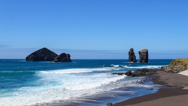 Un paisaje costero con cielo despejado, formaciones rocosas y una playa arenosa.