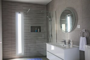A modern bathroom with a glass-enclosed shower, a large mirror, and a white vanity with a towel ring. - Dreamscape Villa (Ponta Delgada)