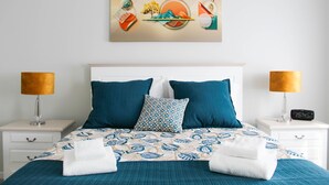 Una cama bien hecha con un edredón estampado, dos almohadas y dos mesitas de noche con lámparas y un reloj.