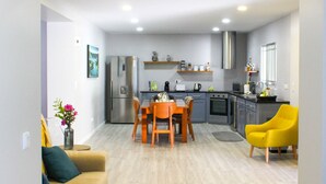 Una sala de estar moderna con sofá, una mesa de comedor con sillas, una zona de cocina con electrodomésticos y un sillón amarillo.
