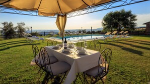An outdoor dining area with a table set for six, overlooking a swimming pool and a scenic view.