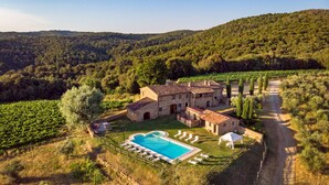 A stone villa with a swimming pool, surrounded by vineyards and a hilly landscape.