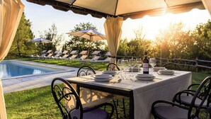 Un área de comedor al aire libre con piscina, sombrillas y sillones de descanso.