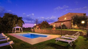 Zona de piscina con sillones de descanso, un pabellón y un edificio de piedra.