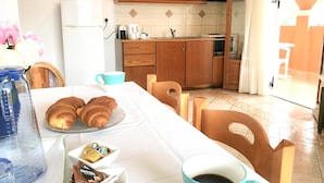 A breakfast setup with croissants, coffee, and a water bottle on a table in a room with wooden cabinets and a tiled floor.