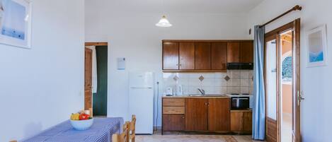 A compact kitchen with wooden cabinets, a dining table with a checkered tablecloth, and a small refrigerator.