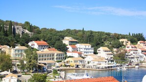 A coastal town with buildings along the waterfront, a marina with boats, and a hill with trees in the background.