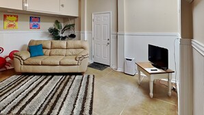 Una sala de estar con un sofá color beige, un tapete a rayas, un televisor sobre una mesa de madera y un ventilador de techo.