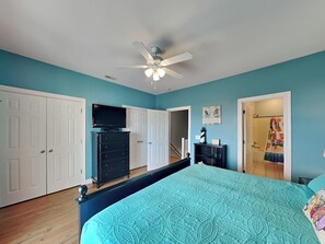 A bedroom with a bed, a ceiling fan, a TV, and a door leading to a bathroom. - Lucky Ducky | Easy Walk to Beach + Pet Friendly! (Carolina Beach)
