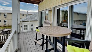 Une terrasse extérieure couverte, dotée d’une table ronde et de chaises, d’une porte-fenêtre coulissante et offrant une vue sur les maisons voisines.