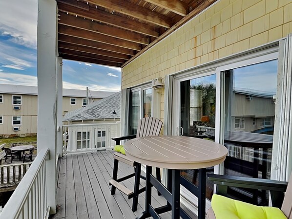 Une terrasse extérieure couverte, dotée d’une table ronde et de chaises, d’une porte-fenêtre coulissante et offrant une vue sur les maisons voisines.