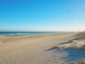 Een breed zandstrand met zachte golven en een heldere lucht.