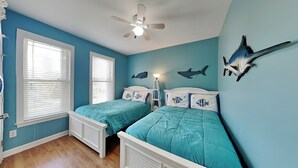 Un dormitorio con dos camas, ventilador de techo y decoraciones de pared con motivos de peces y tiburones.