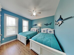 Een slaapkamer met twee bedden, een plafondventilator en wanddecoraties met vis- en haai-motieven.
