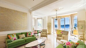 Un salón amplio con un conjunto de sofá verde, una mesa de centro y vistas al mar a través de amplios ventanales.