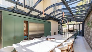 Una cocina moderna con una isla grande, armarios verdes y un área de patio con paredes de vidrio.